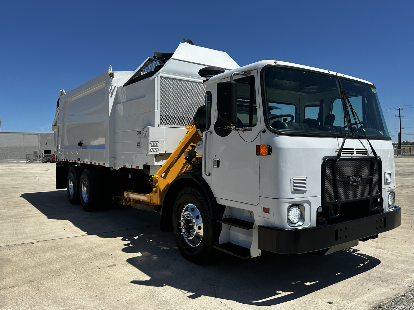 Autocar XPEDITOR garbage truck in-service showing side-mounted hopper and grim-retraction arm with hydraulic mechanism and dump body.