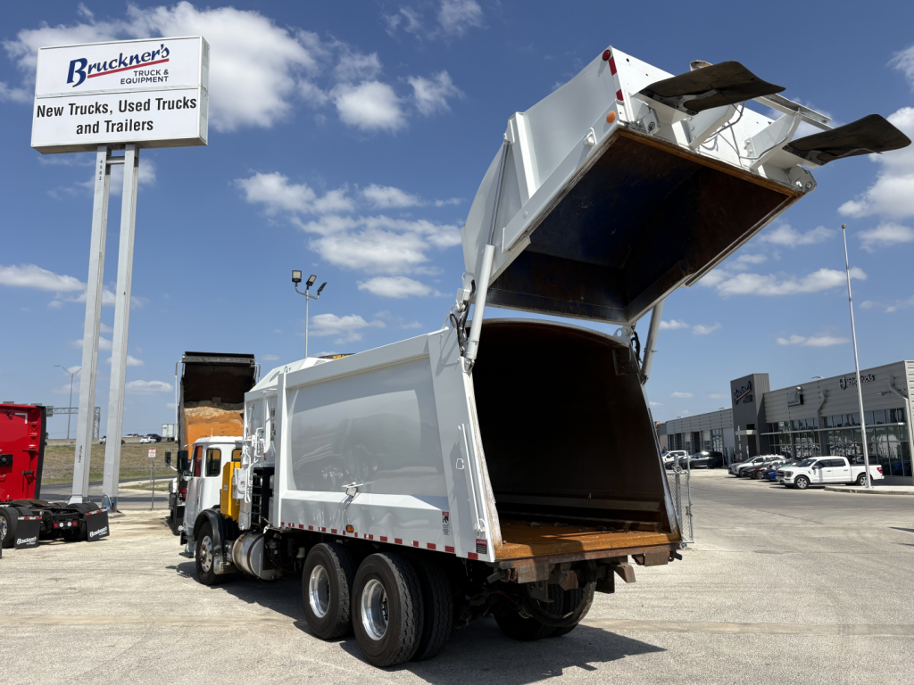 Truck rear with dump bed raised showing empty cargo bed and hydraulic mechanism, Autocar XPEDITOR model likely, white dump truck with black undercarriage and dual rear axles.