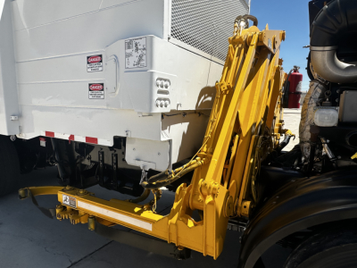 Truck rear with yellow hydraulic telescoping arm/crane attachment and white body, warning labels on panel, wheels visible.