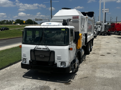 Autocar XPEDITOR truck with garbage body, front view. Visible text includes HELI on side, Axle/Chassis components, and a small sticker on windshield.