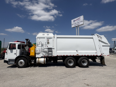 Autocar XPEDITOR garbage truck side view showing large white dump body and three rear wheels, with cab on the left and signage in background.