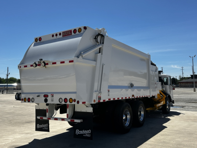 Rear view of a white dump truck with a raised bed, showing taillights, lights, and a Brackner’s plate; no visible text legible except small HEIL logo on top of bed and license/branding at rear.