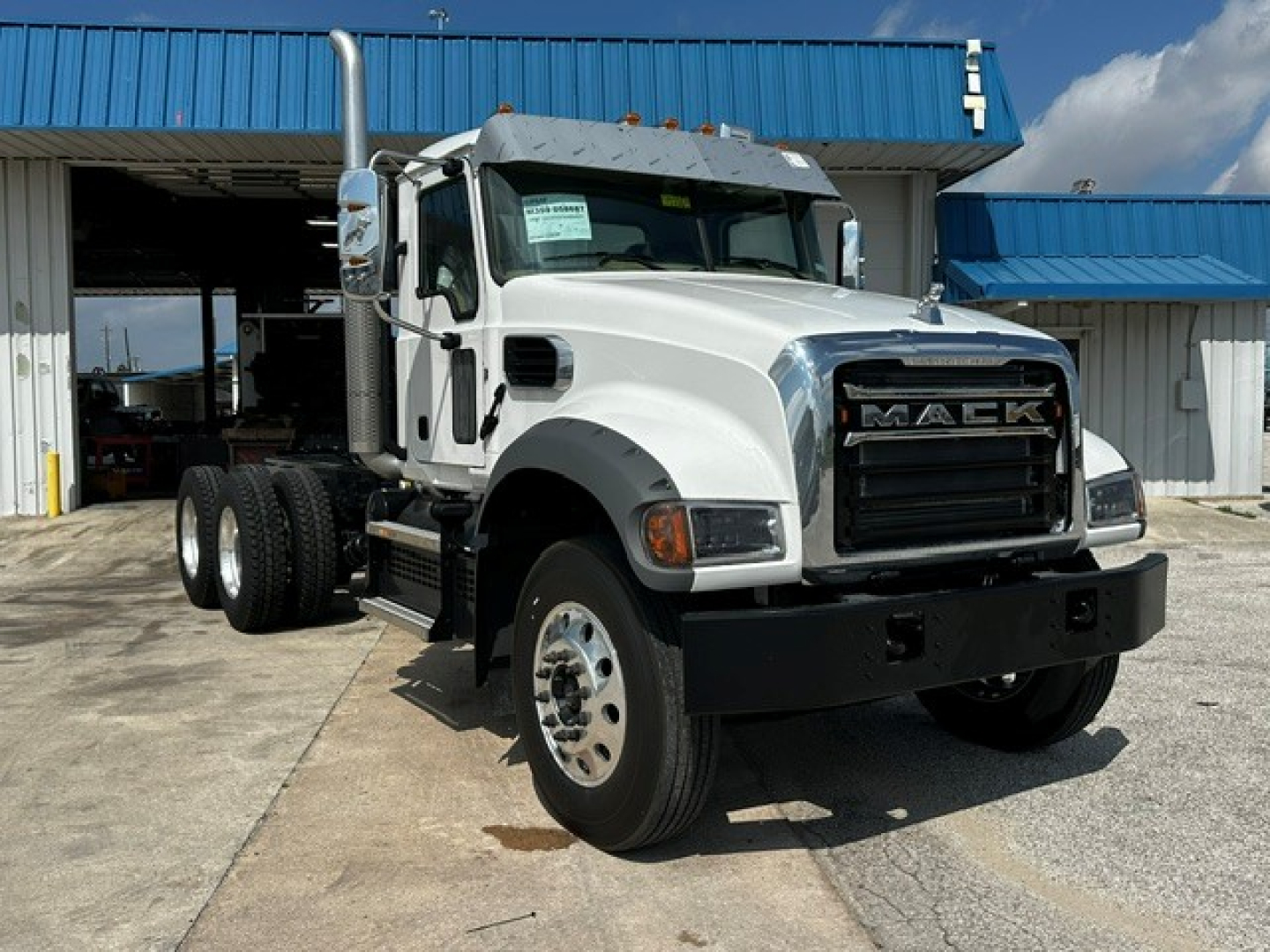 Truck cab and chassis showing Mack GR64F front grille and white body, dual rear wheels, black bumper, chrome exhaust stacks, daytime.