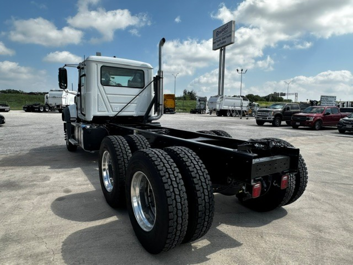 Truck chassis showing rear dual rear axles and Mack GR64F cab in white with black frame and wheels.