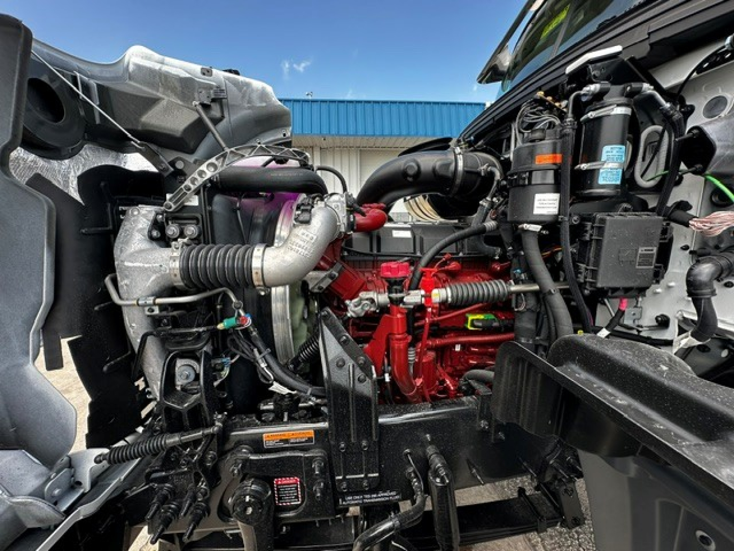 Mack GR64F engine bay and chassis showing turbocharger, red engine block, hoses, and various components.