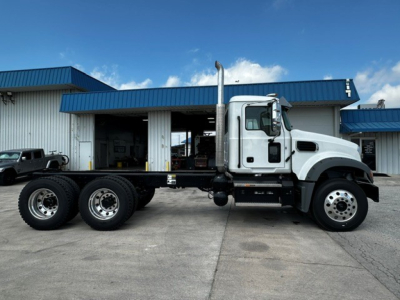 Truck side view showing 2027 Mack GR64F cab and chassis with three rear axles and dual exhaust stack.
