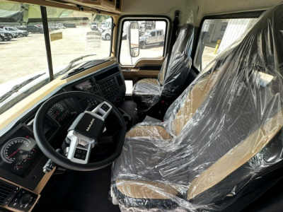 Cab interior of new 2027 Mack GR64F showing tan and black seats wrapped in plastic, steering wheel, dashboard, and large windows.