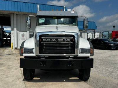 Mack GR64F cab and chassis front view showing large black grille with MACK lettering, white cab, rectangular headlights, and heavy front bumper.