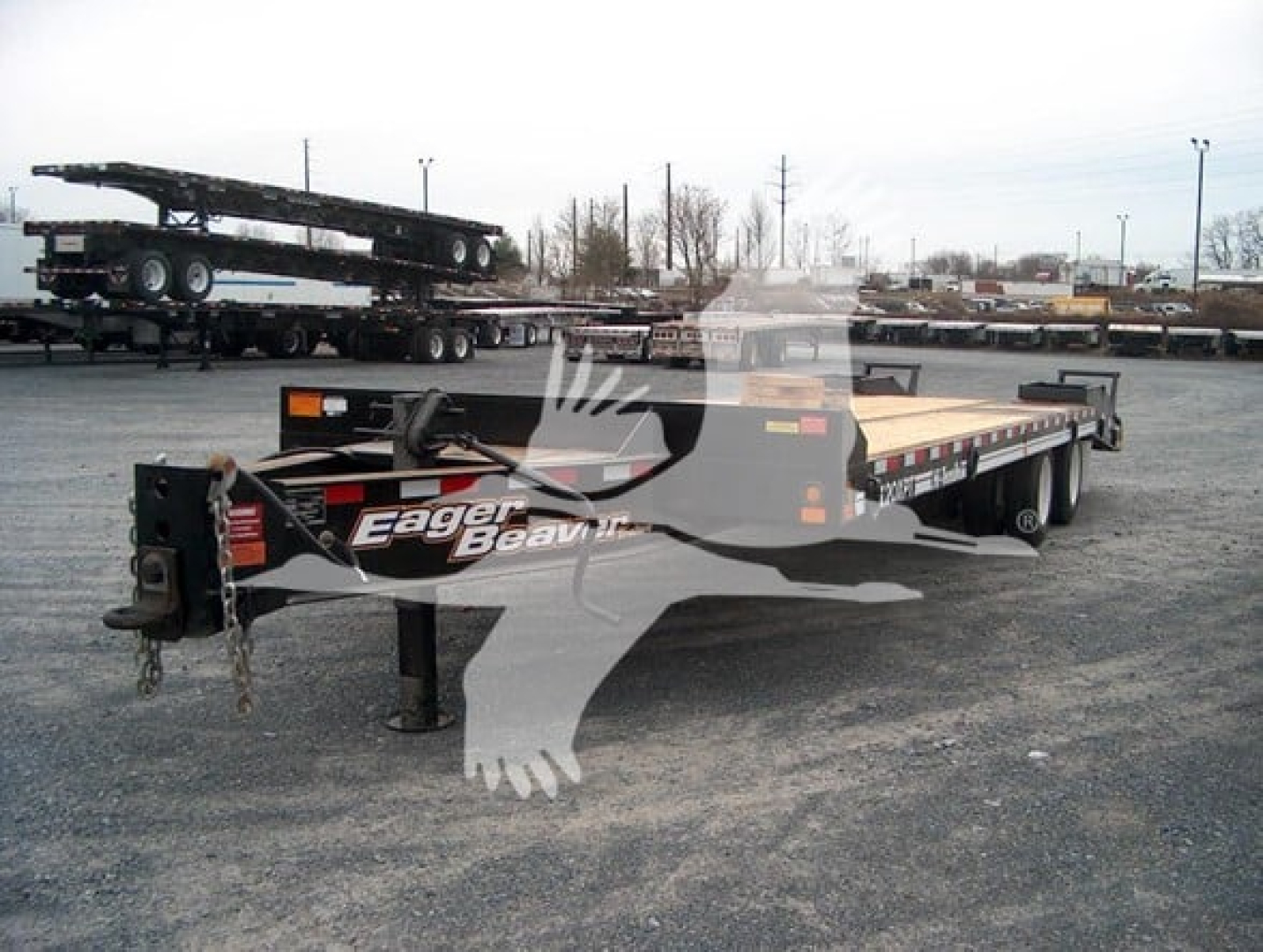 Flatbed trailer by Eager Beaver with gooseneck, black/gray color, showing dual-level decking and landing gear, with Eager Beaver logo on the front.