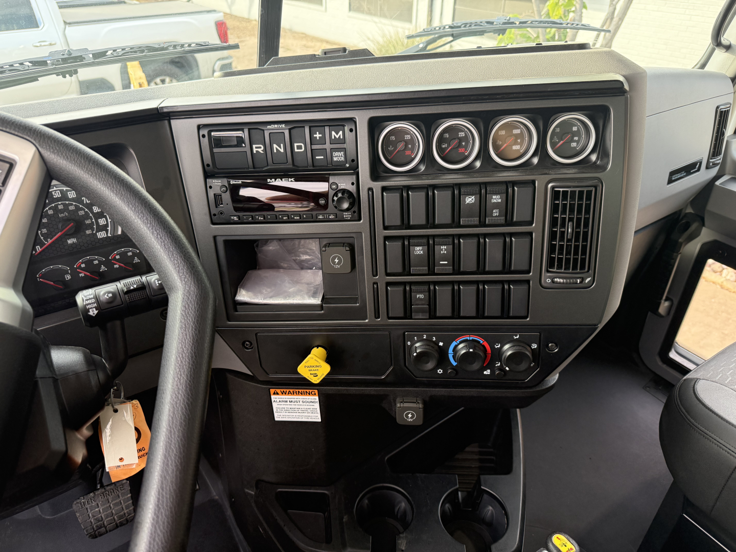 Dashboard view of a 2026 Mack GR64F truck showing instrument cluster, climate controls, and gear selector with labels.