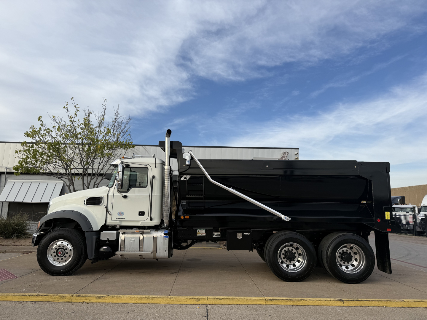 Truck in-service Mack GR64F dump truck side profile showing black dump bed, white cab, chrome exhaust stack, and dual rear axles.