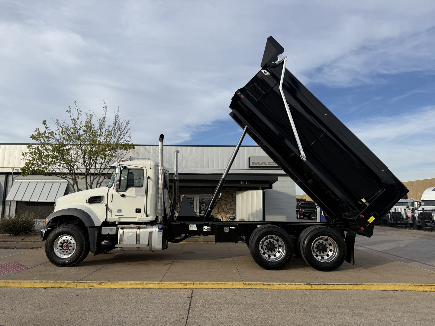 2026 Mack GR64F dump truck side profile showing dump body raised on hydraulic cylinders with three rear axles and white cab.