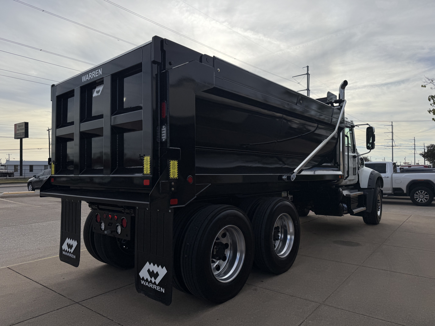Dump truck rear/side view showing Warren dump body and dual rear axles on a black Mack GR64F.