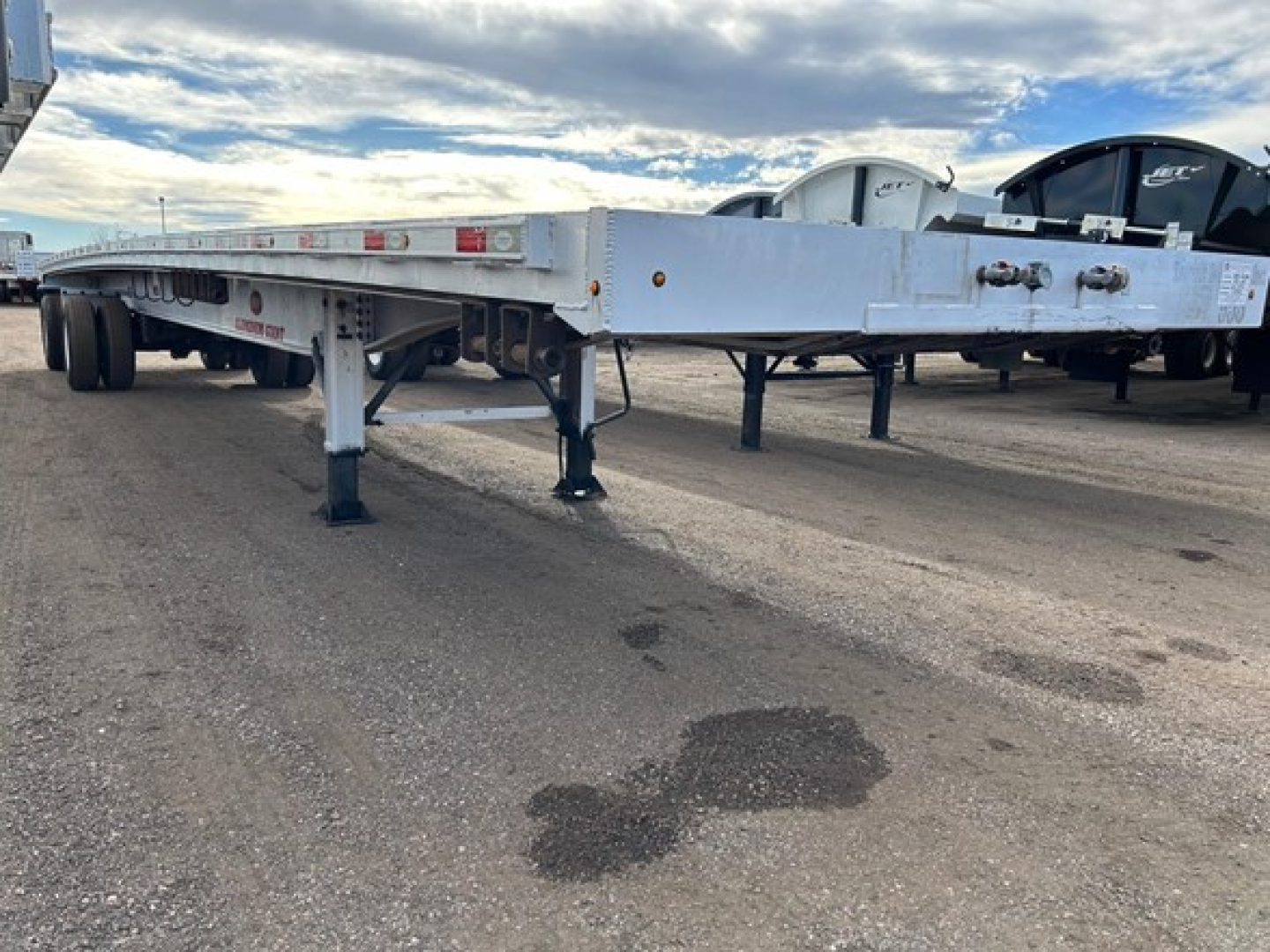 Trailer underside and frame showing flatbed trailer with legs extended, aluminum deck, side rails, and support jacks visible.