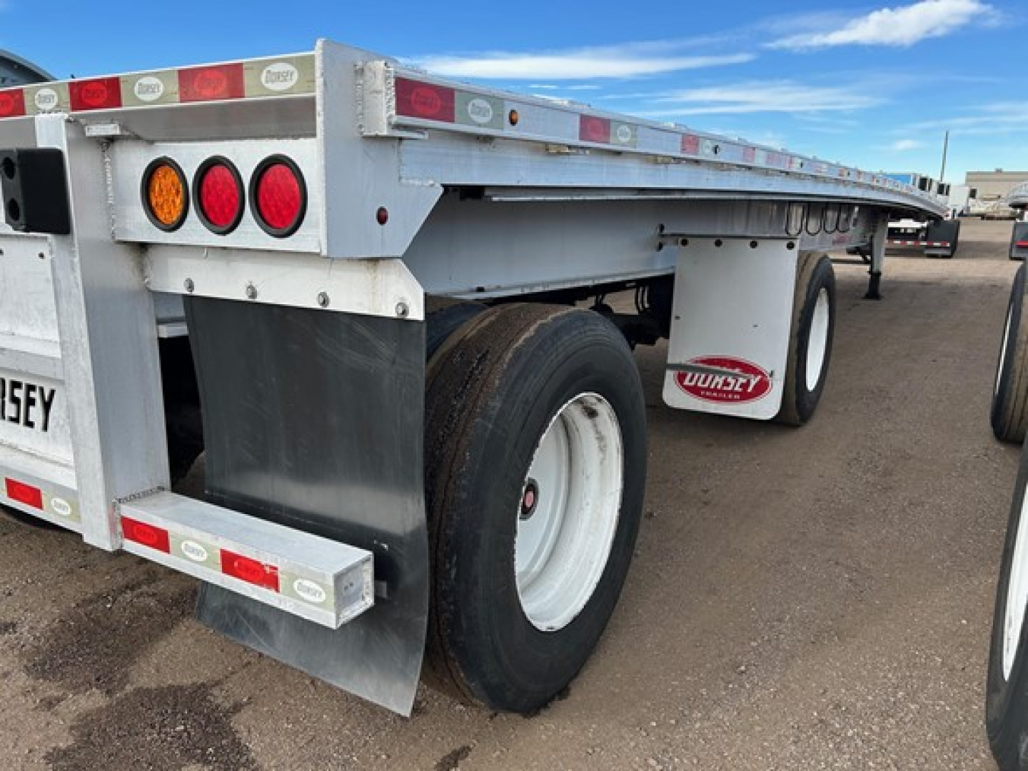 Trailer rear side showing dual rear tires and flatbed with mud flaps and RUNWAY sticker; tail lights and reflective tape along edge; white wheels and metal frame.