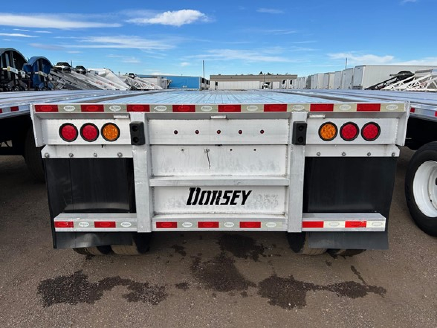 Rear view of a flatbed trailer showing tail lights, mud flaps, and Dorsey logo on the bumper with a white frame and red/white reflective tape.