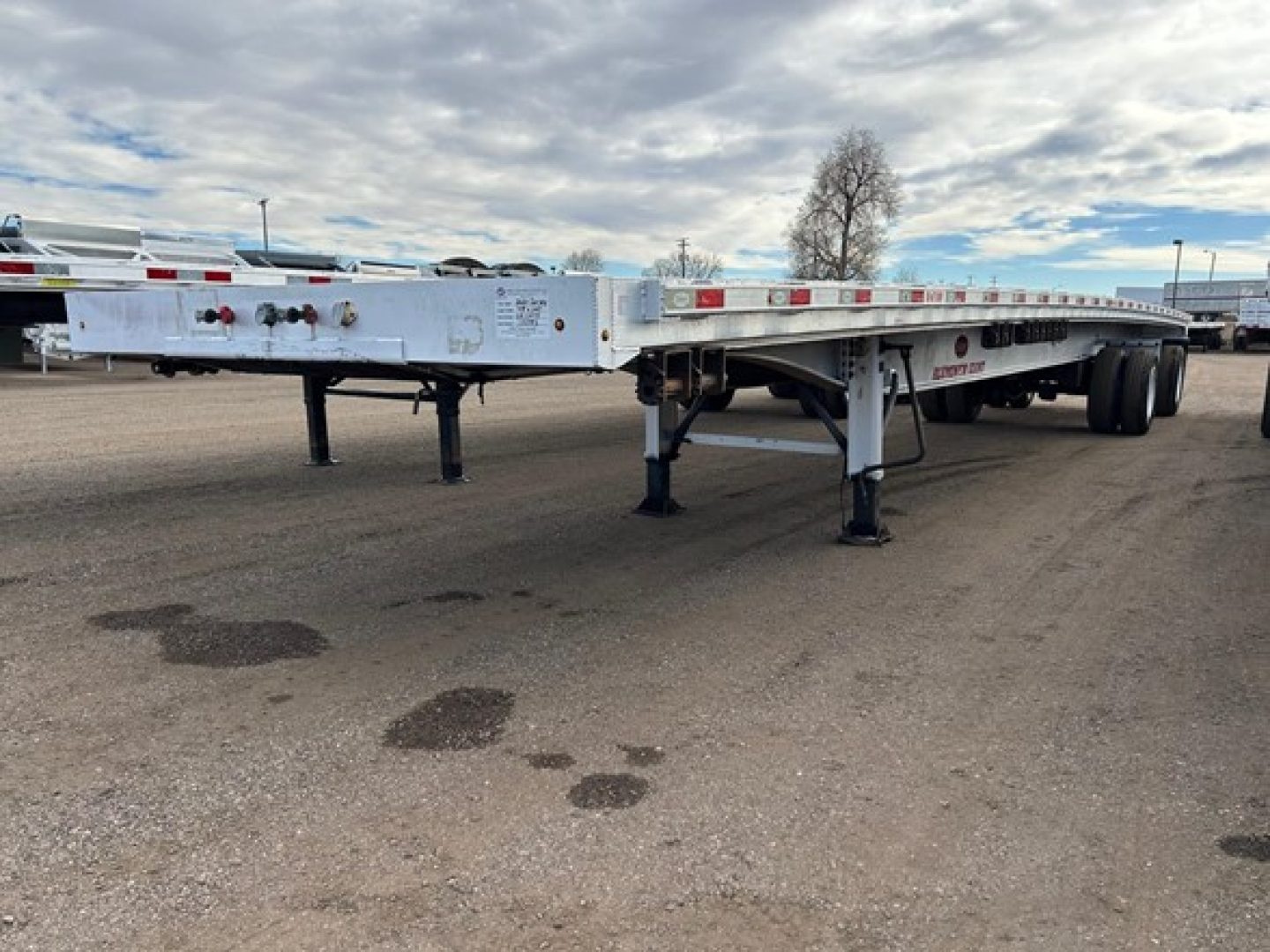 Flatbed trailer showing wheel area and support legs with reflective tape along the sides.
