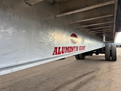 Aluminum Giant trailer side showing ALUMINUM GIANT branding beneath the flatbed overhang and dual rear wheels.