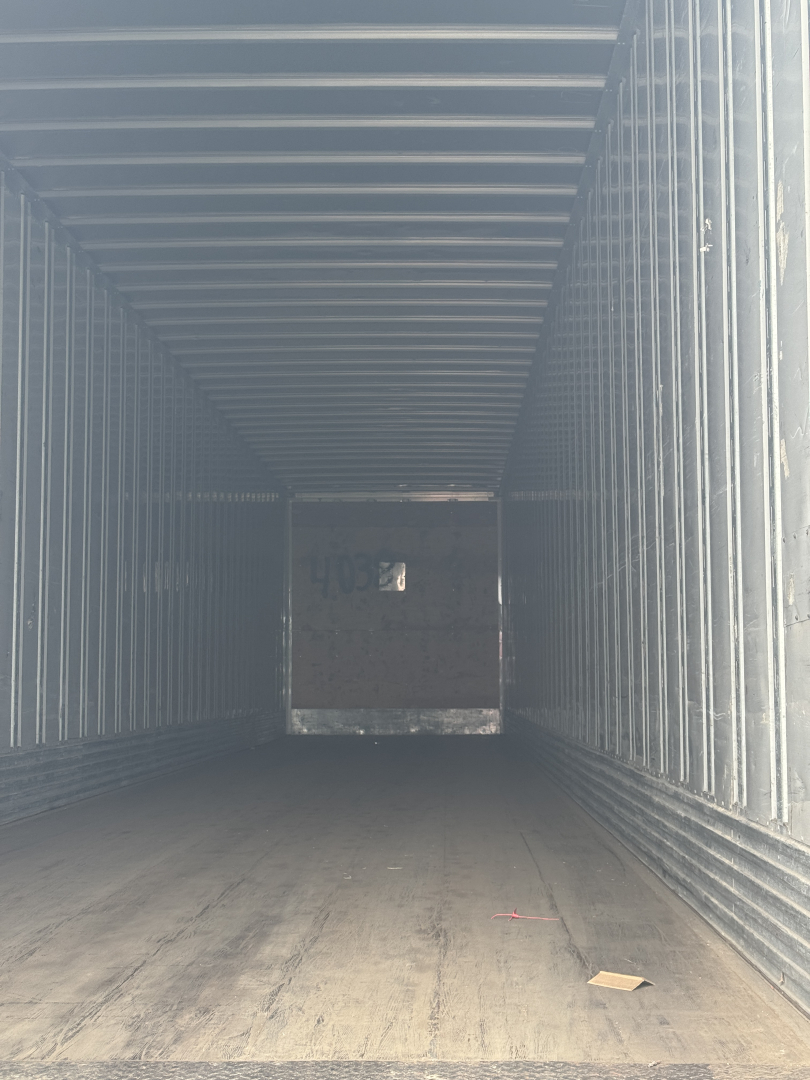 Trailer interior showing empty cargo space with metal sidewalls and a wooden floor; rear door open showing back wall.