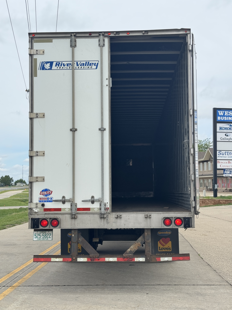 Rear of a utility trailer with open cargo area, River Valley trailer dealership sticker, taillights, bumper, and loading area visible.