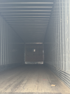 Trailer interior showing empty cargo space with metal sidewalls and a wooden floor; rear door open showing back wall.