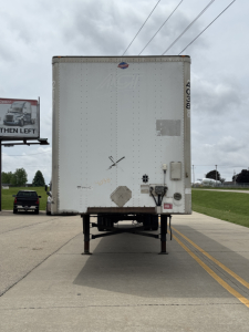 Utility 4000 Dx trailer rear view showing raised legs, rear doors, bumper with lights, and stickers/markings on a paved lot.