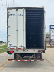Rear of a utility trailer with open cargo area, River Valley trailer dealership sticker, taillights, bumper, and loading area visible.