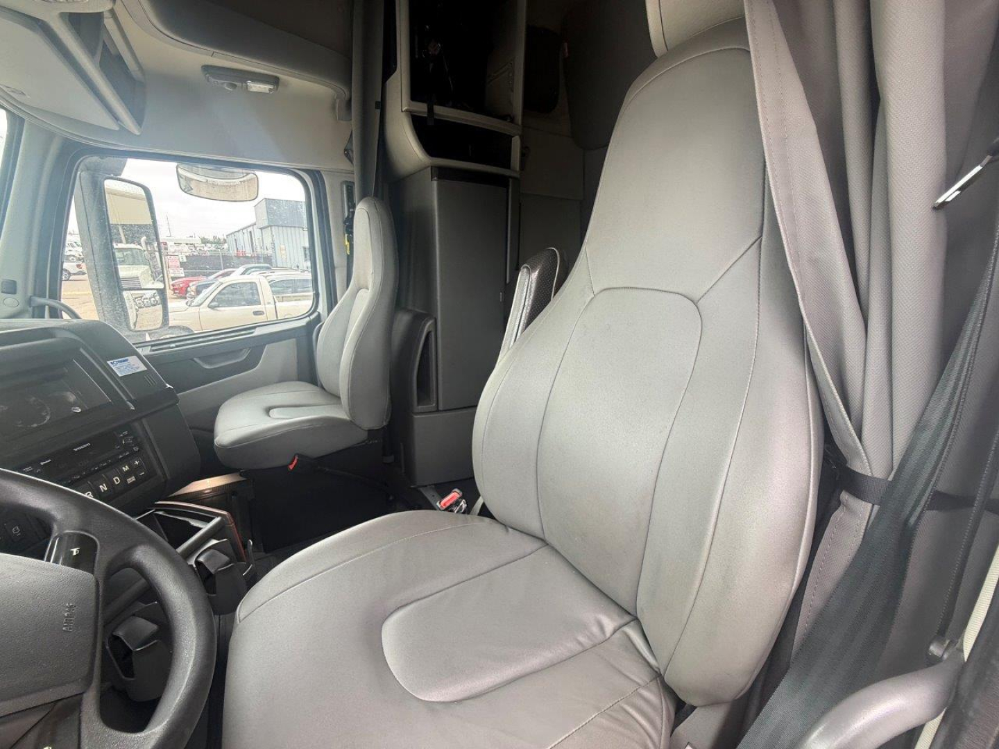 Volvo VNR cabin interior showing driver's seat and passenger seat with gray upholstery, steering wheel, dashboard, and bunk area visible.
