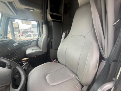 Volvo VNR cabin interior showing driver's seat and passenger seat with gray upholstery, steering wheel, dashboard, and bunk area visible.