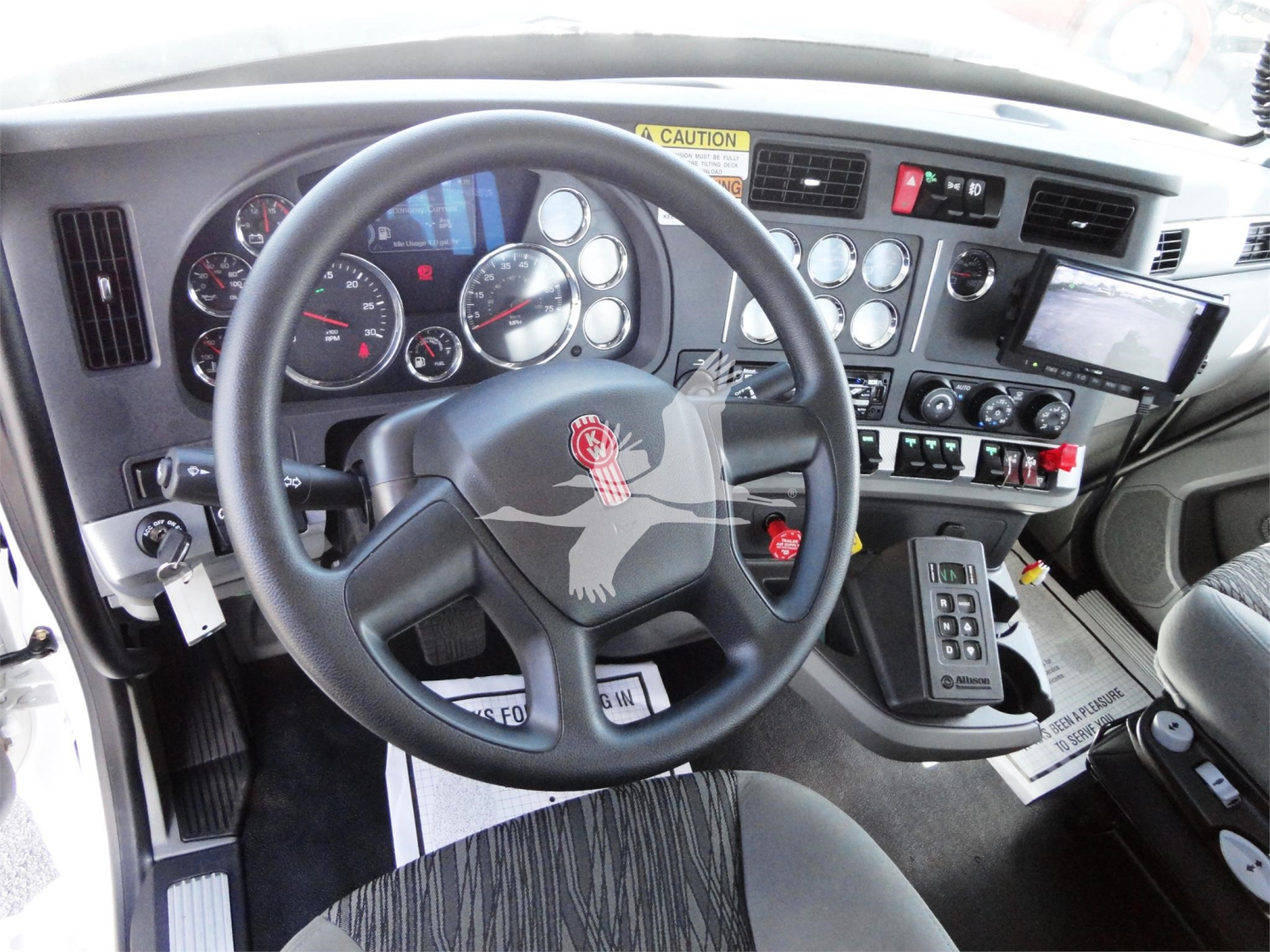 Kenworth W990 cockpit showing steering wheel and dashboard controls with gauge cluster and driver seat.