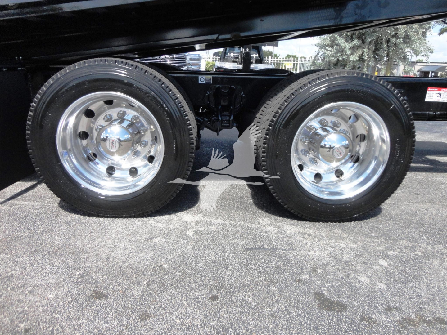 Kenworth W990 side view of dual rear wheels showing shiny chrome rims and suspension undercarriage.