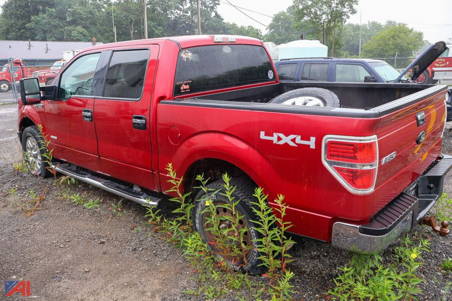 Side view of a red 2011 Ford F-150 pickup with 4x4 badge, quad cab, and bed; VIN plate not visible; truck parked on gravel with weeds nearby.