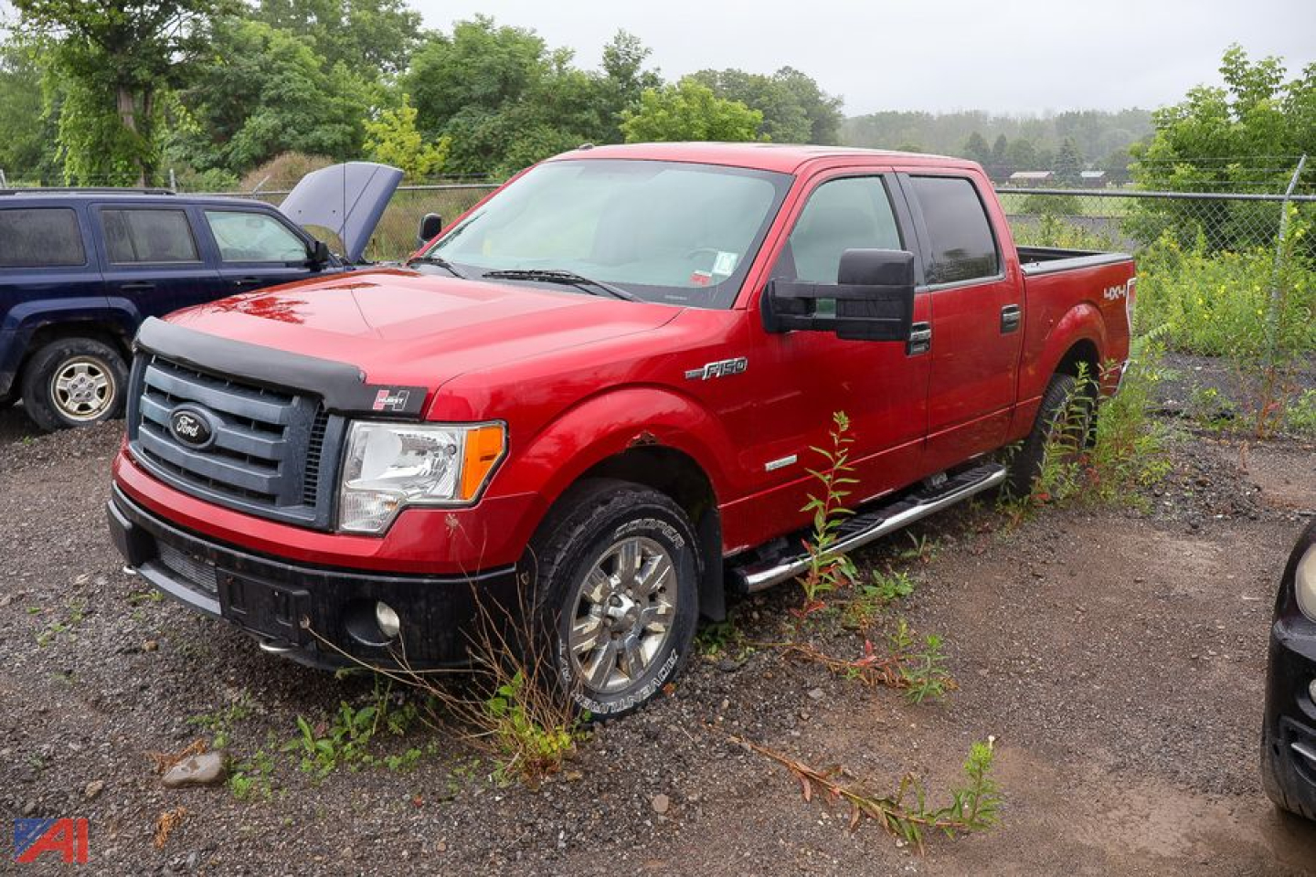 Ford F-150 pickup truck in red, extended cab 4x4, with crew cab, showing front grille and side mirrors, outdoor lot.