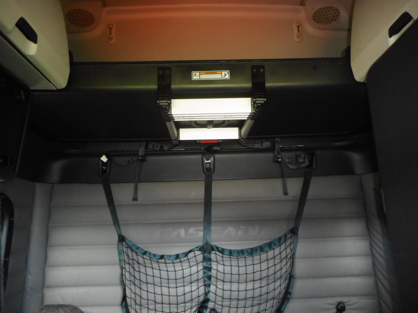 Freightliner Cascadia interior cargo area showing seat belt straps and netting in the cab, with storage hatch and overhead panel.