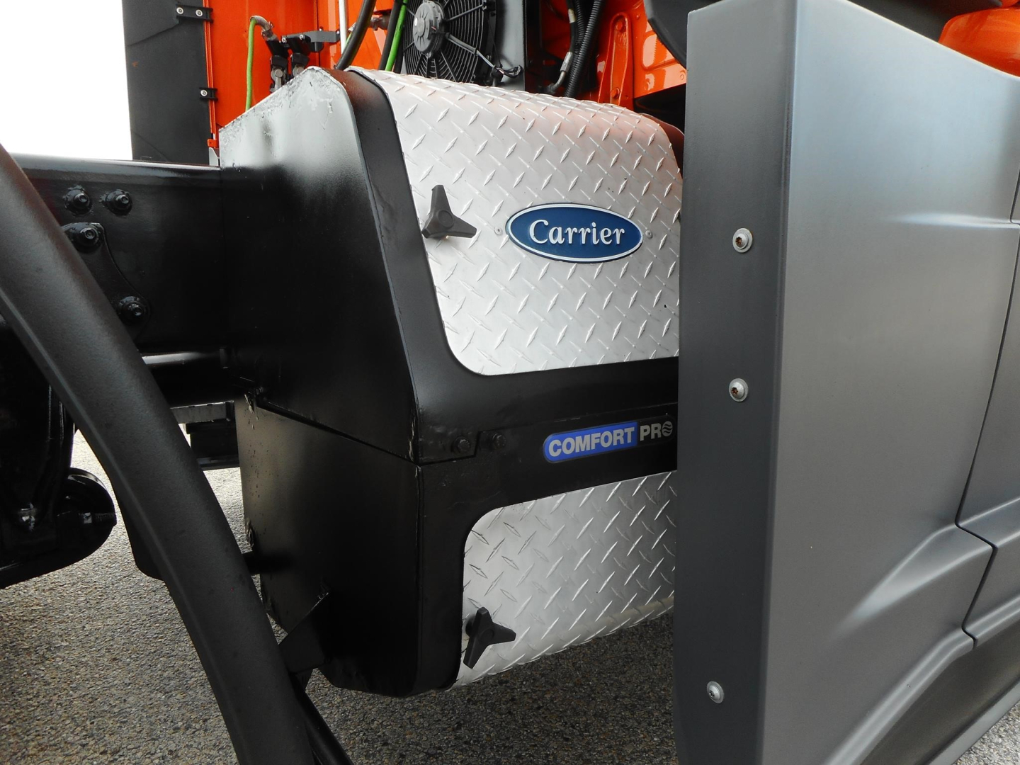 Truck engine bay area showing Carrier Comfort Pro cooling unit with diamond plate panel and surrounding components on a Freightliner Cascadia.
