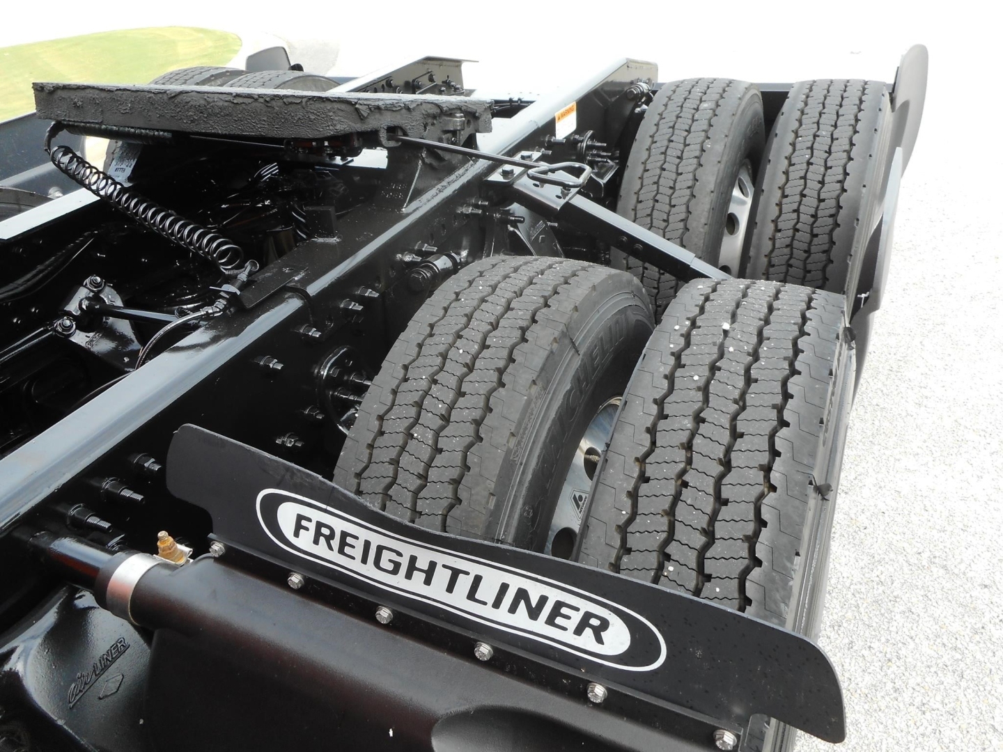 Freightliner Cascadia truck chassis showing dual rear axles, tires, and frame with Freightliner mudflap logo.