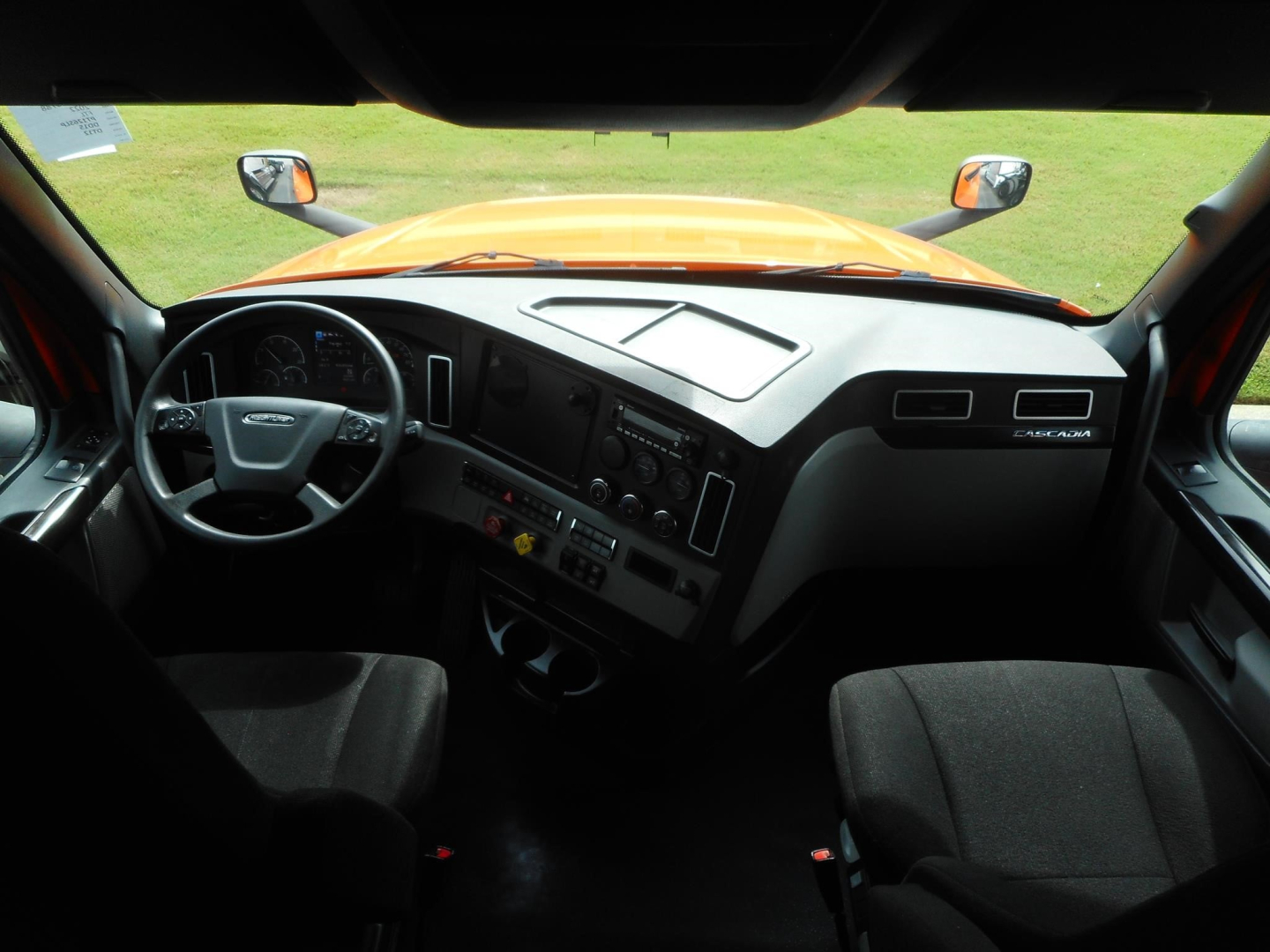 Dashboard and steering wheel area of a Freightliner Cascadia cab interior. Visible texts include 'FREIGHTLINER' on dash badge, instrument cluster, center console with controls, air vents, and a glovebox area.