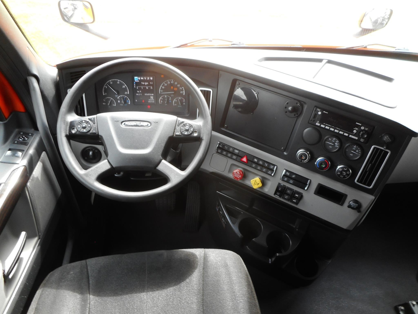 Freightliner Cascadia truck interior driver’s area showing steering wheel and dashboard with gauges, center console, and control panel.