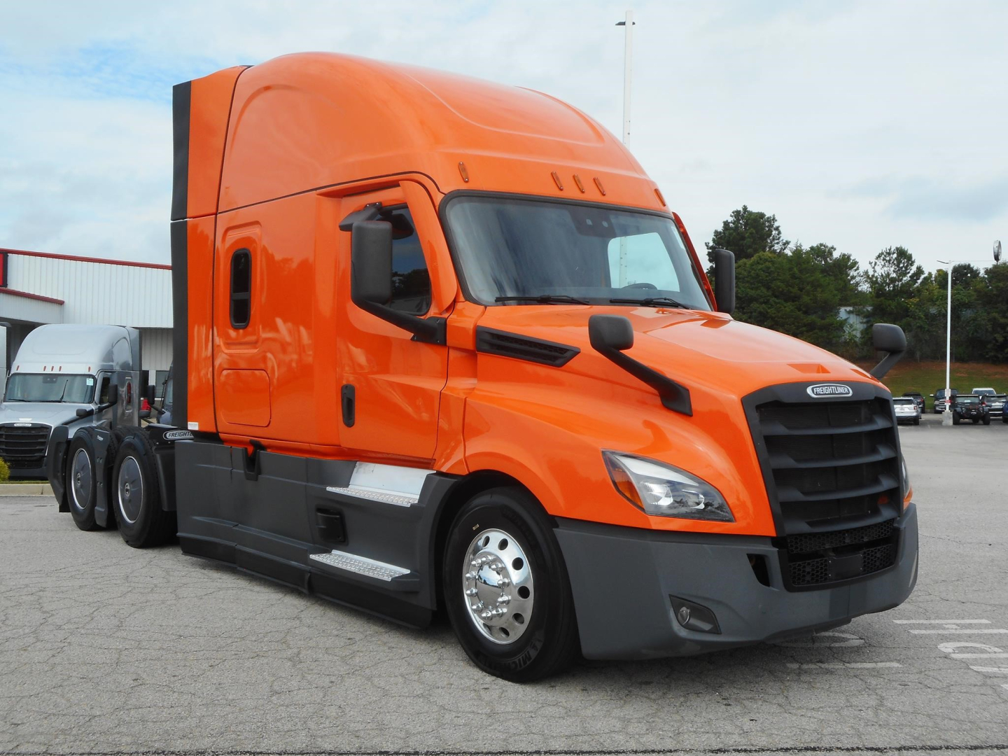Freightliner Cascadia tractor head showing bright orange cab and black grille.