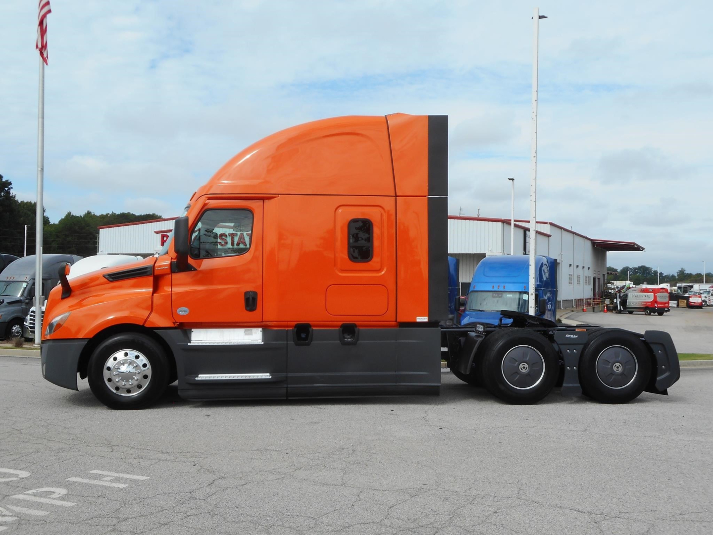 Freightliner Cascadia semi-truck tractor in orange with sleeper cab, side view showing the cab, wheels, and chassis.