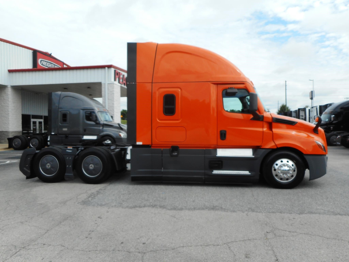 Freightliner Cascadia sleeper cab tractor in orange, side view showing exterior doors, chrome exhaust, and wheel assemblies.