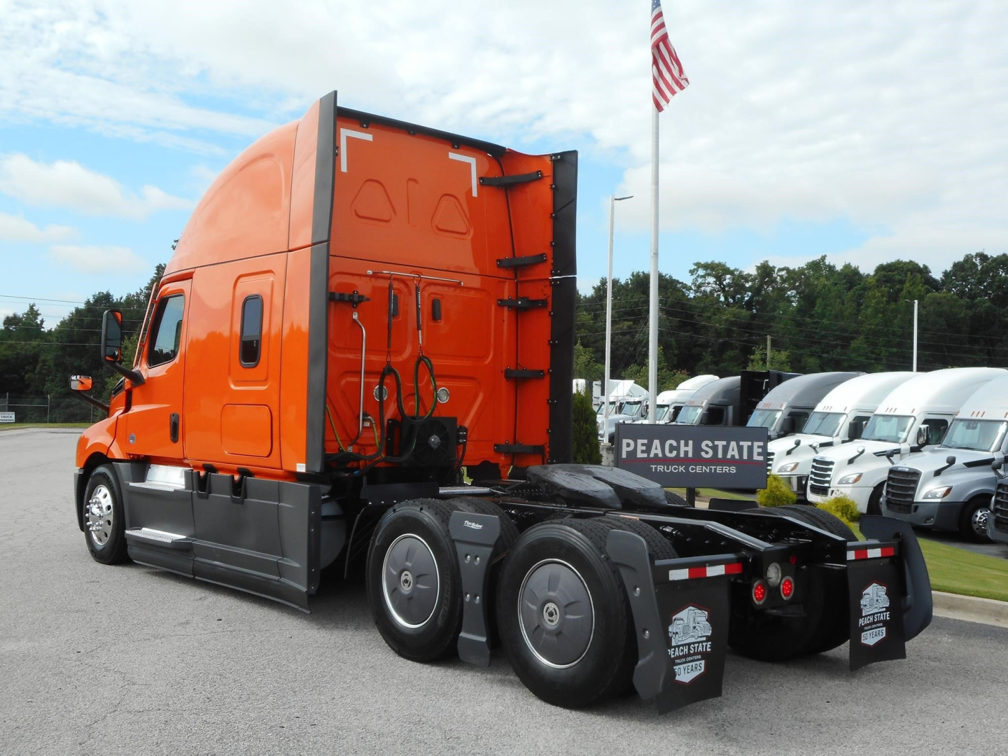 Freightliner Cascadia truck tractor rear and side view showing orange cab and black chassis with fifth-wheel and dual rear axles.