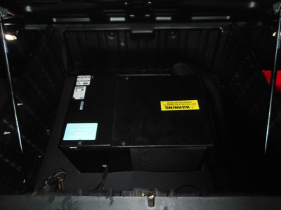 Trucks engine bay showing a large black battery/auxiliary unit with warning label and blue sticker in the cargo area.