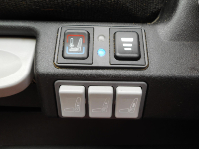 View of cabin controls in a Freightliner Cascadia showing seat heater and three seat adjustment switches plus a blue indicator, front panel details.