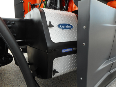 Truck engine bay area showing Carrier Comfort Pro cooling unit with diamond plate panel and surrounding components on a Freightliner Cascadia.