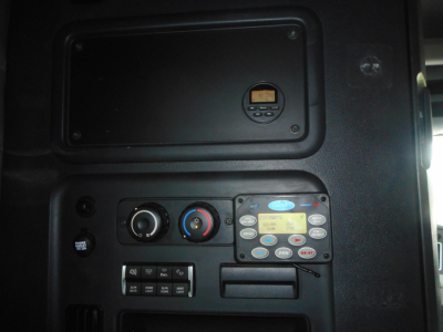 Dashboard panel of a Freightliner Cascadia showing climate controls and a small gauge, along with a digital control keypad and storage hatch.