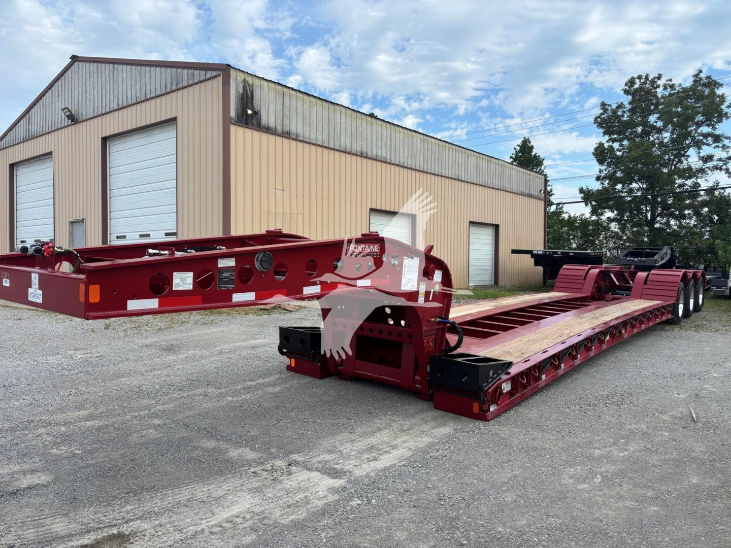 Fontaine 55 LCC lowboy trailer in red with detachable gooseneck and dual rear axles parked outside a beige building.
