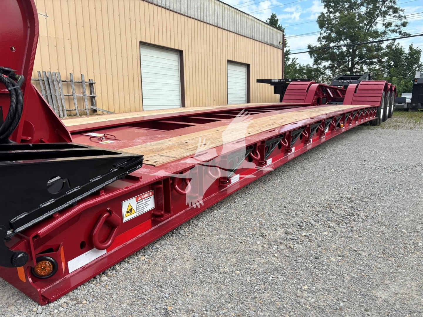 Lowboy trailer by Fontaine 55 Lcc showing long red frame, wooden deck, multiple axles at rear, warning labels, and VIN plate area visible.
