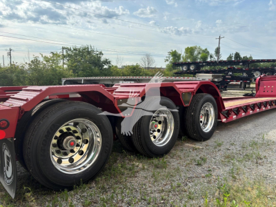  Fontaine 55 Lcc lowboy trailer showing black tires with chrome rims and red frame under clear sky.