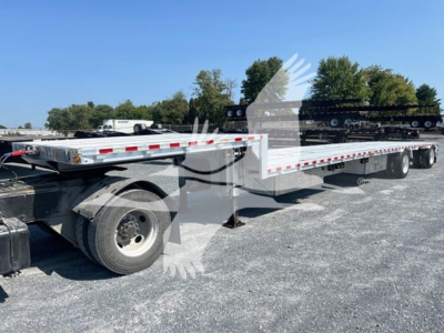 Flatbed trailer showing long drop deck with tandem axles and Steerable landing gear, white with red reflectors.
